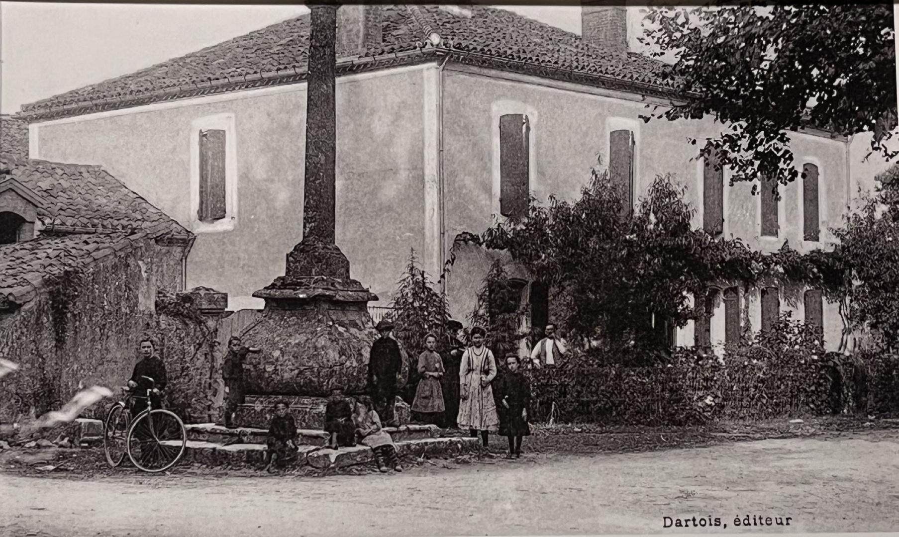 photo ancienne où l'on peut voir plusieurs adultes et enfants autour de la croix Louis XIV et devant l'ancien presbytère
